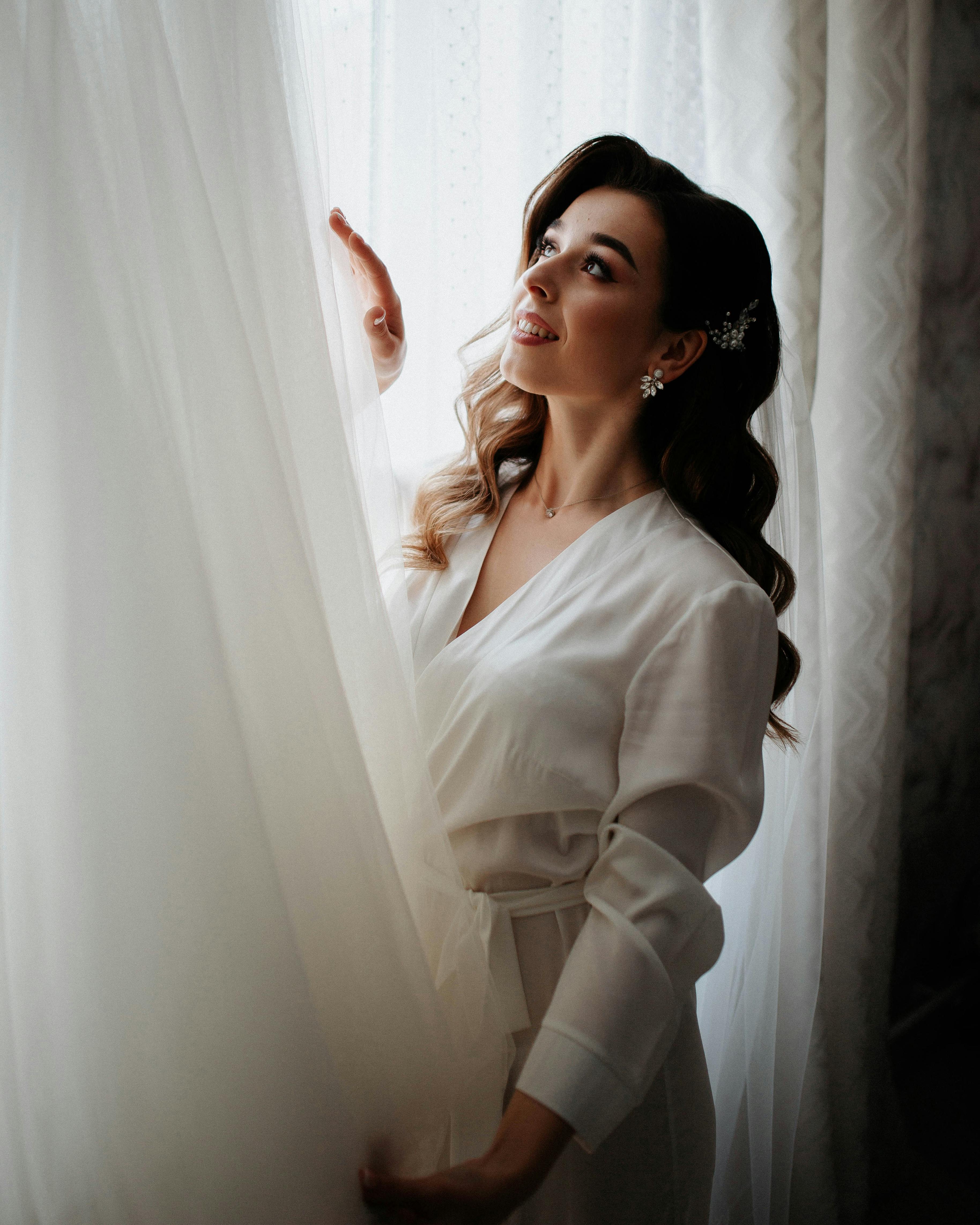 A bride smiling at her wedding dress indoors | Source: Pexels