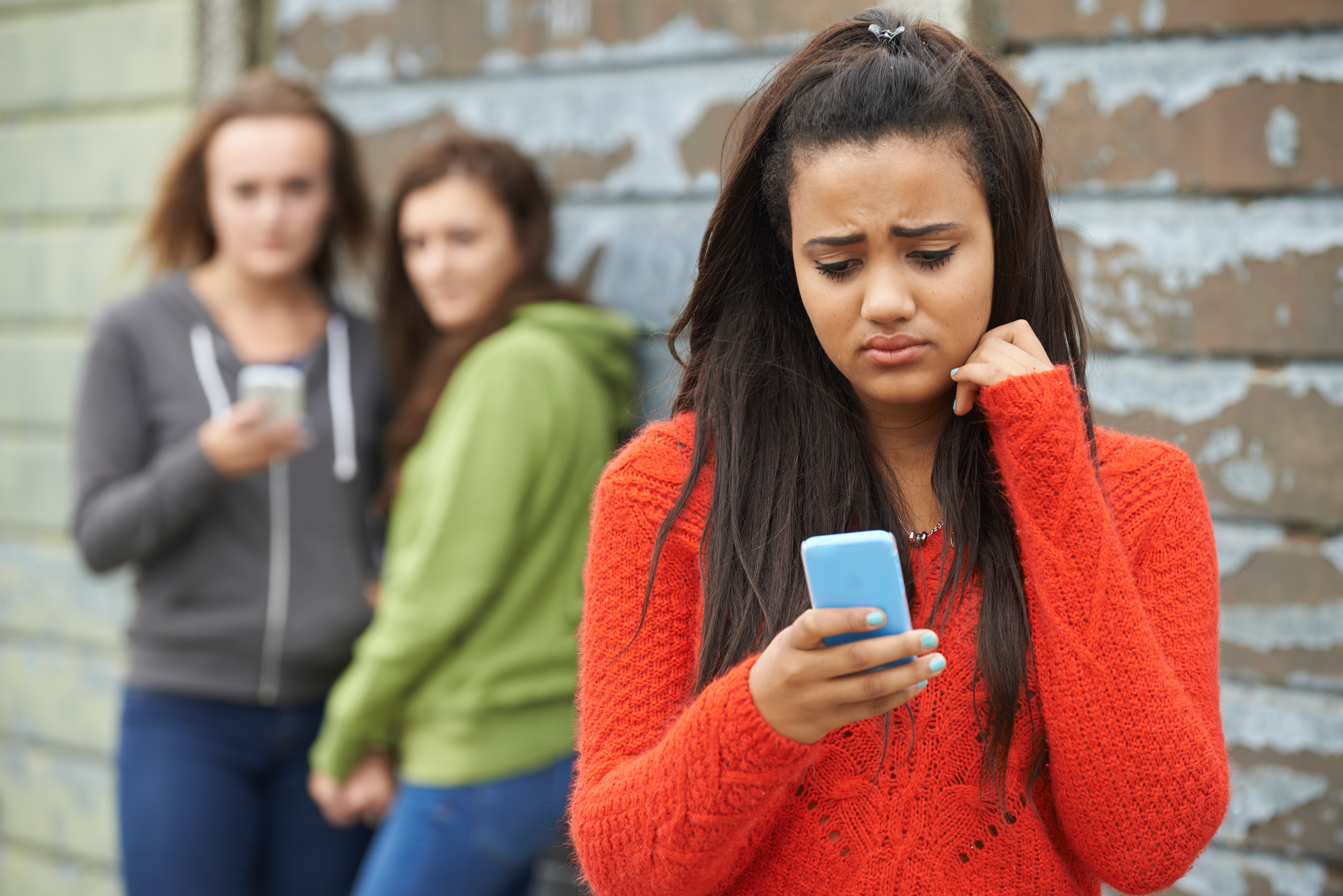 A girl looking worried as two other girls watch her behind | Source: Shutterstock